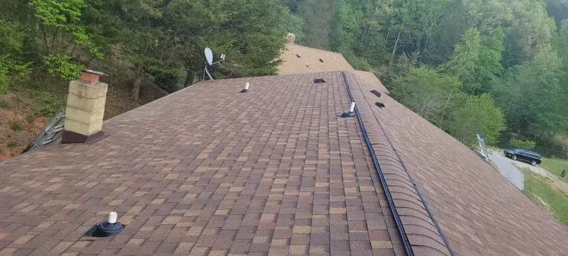 Brown architectural shingle roof with a brick chimney and wooded hills behind