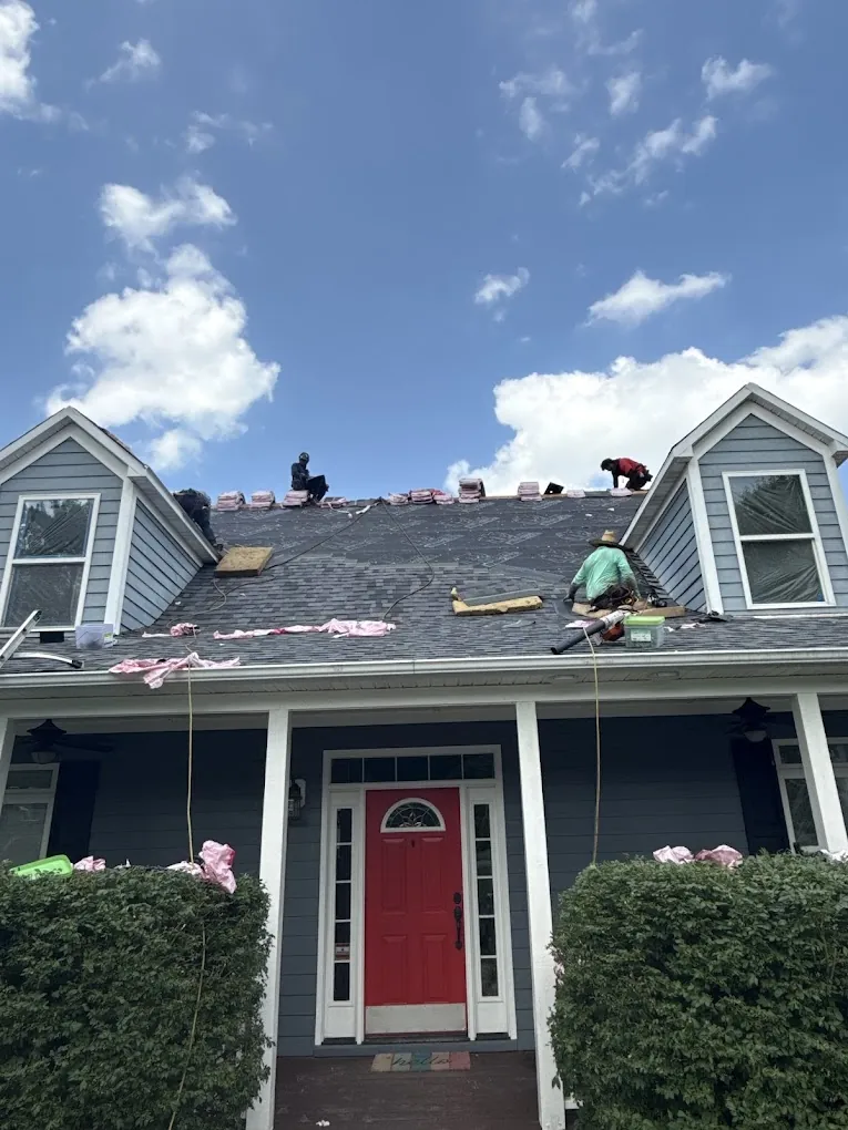 Roofers working on the roof of a two-story house with a red front door and dormer windows