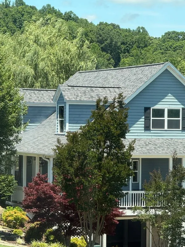 A finished gray shingle roof on a two-story house with light blue siding and a covered porch