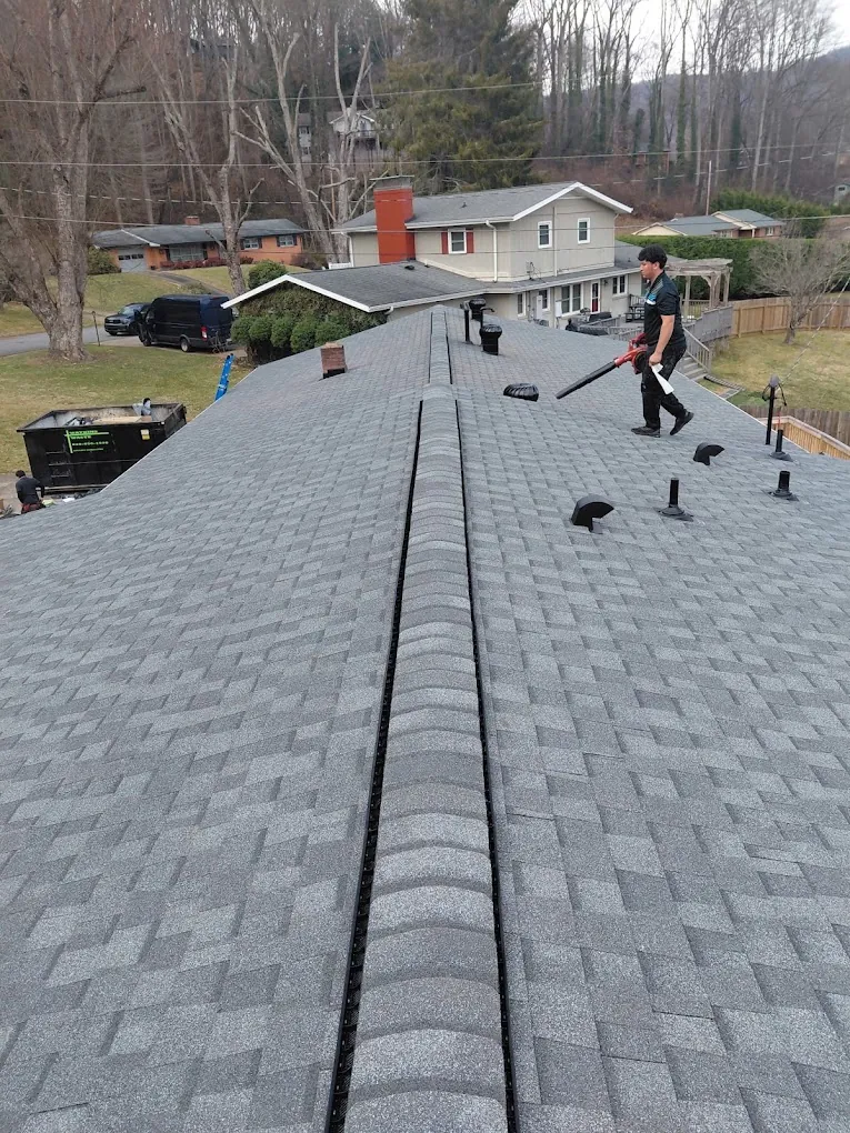 Crew working along the ridge of a new gray shingle roof above a neighborhood street